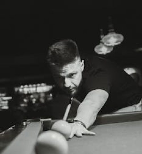 Black and white image of a man concentrating during a billiards game, illustrating intense focus.